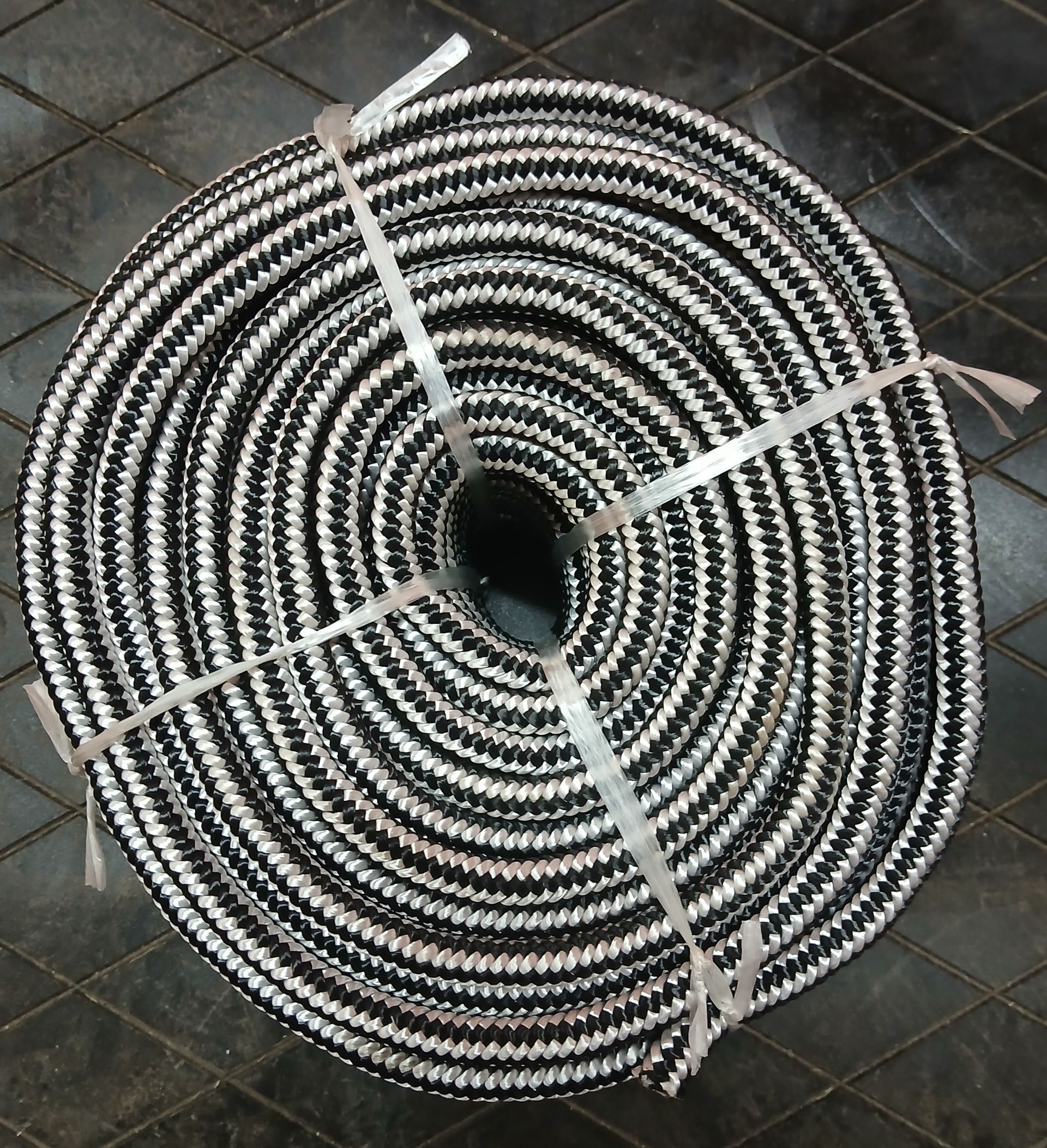 Coiled black and white rope, secured with white plastic straps, resting on a dark surface. Coiled black and white rope, secured with white plastic straps, resting on a dark surface.