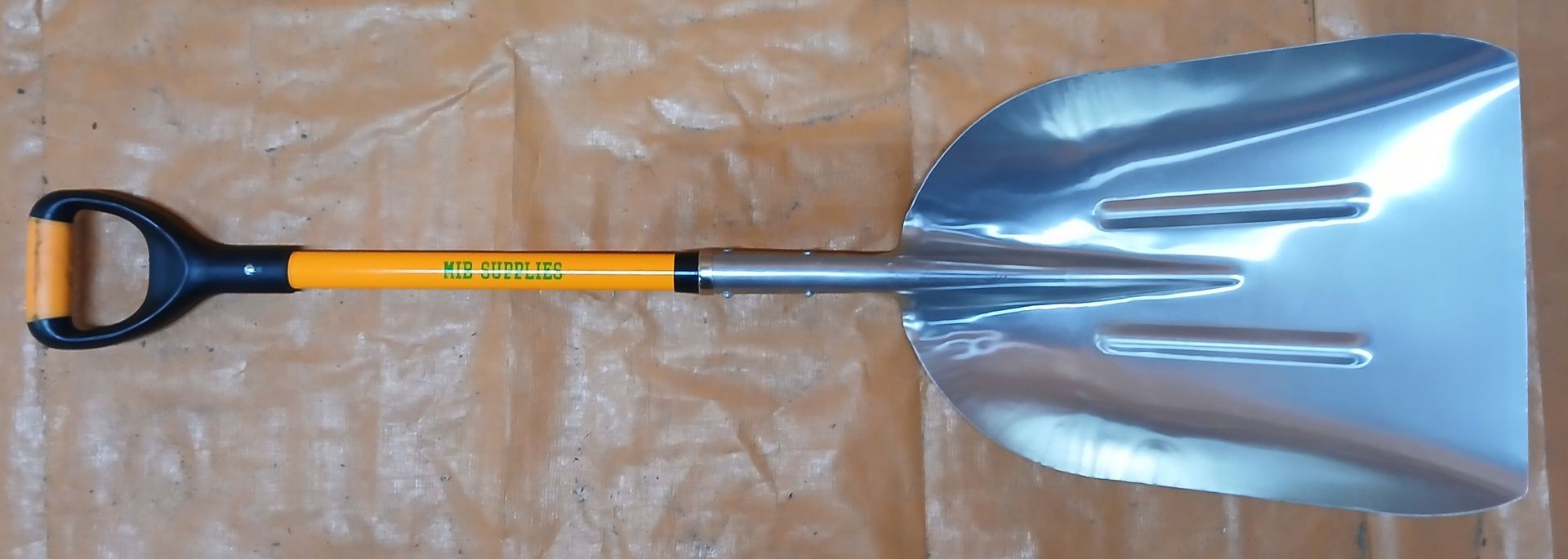 Snow shovel with a silver blade and yellow handle, lying on a brown surface. Snow shovel with a silver blade and yellow handle, lying on a brown surface.