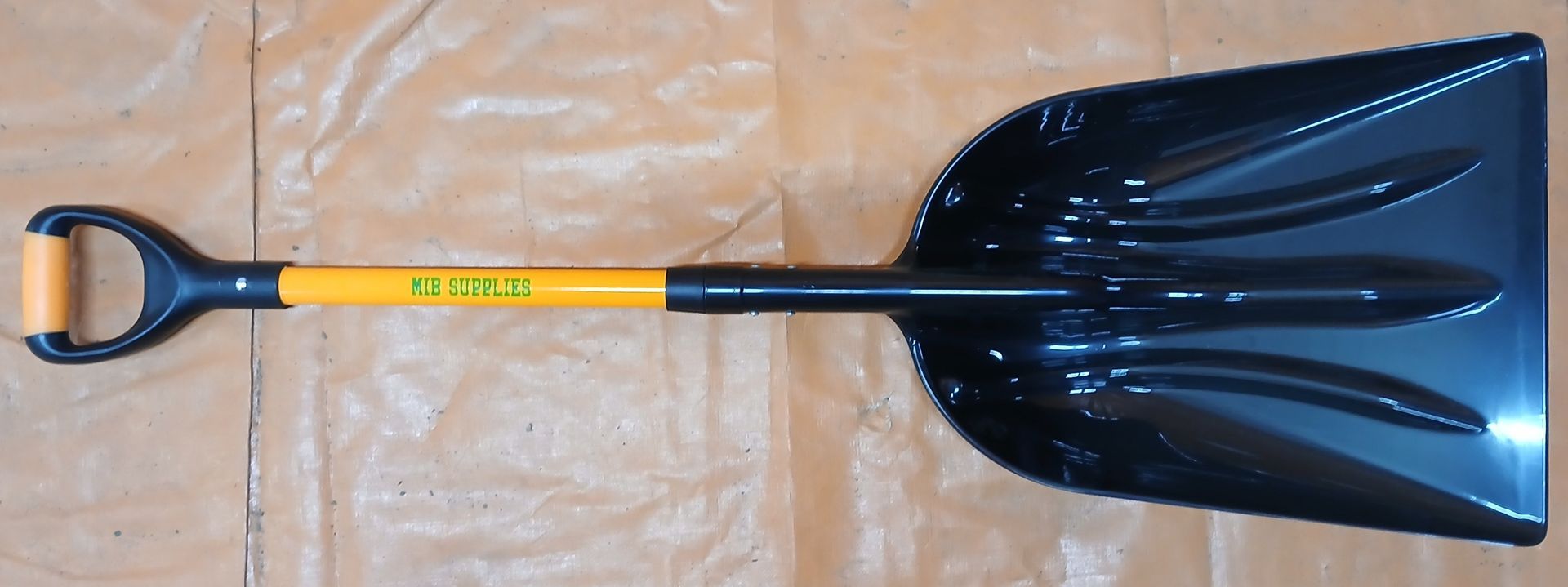 Black and yellow snow shovel on a brown surface. Black and yellow snow shovel on a brown surface.