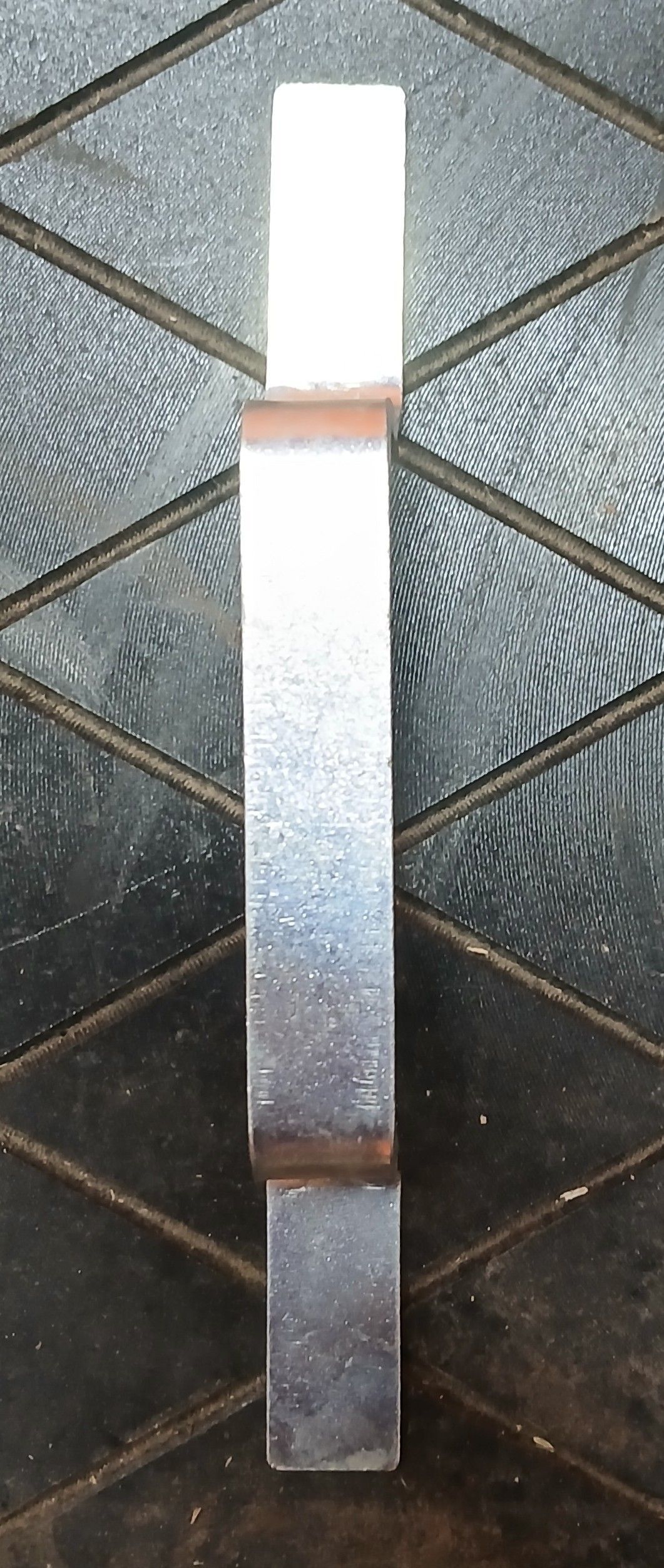 Metal specimen with two sections joined with visible weld, resting on a textured surface.