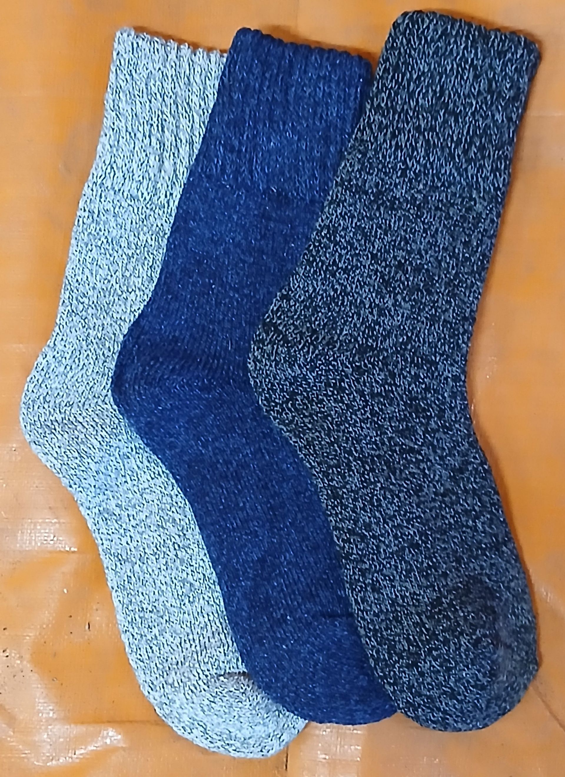 Three thick, knitted socks in shades of blue and gray on an orange surface. Three thick, knitted socks in shades of blue and gray on an orange surface.