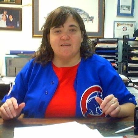 Woman in a Chicago Cubs jersey, sitting at a desk, looking forward.