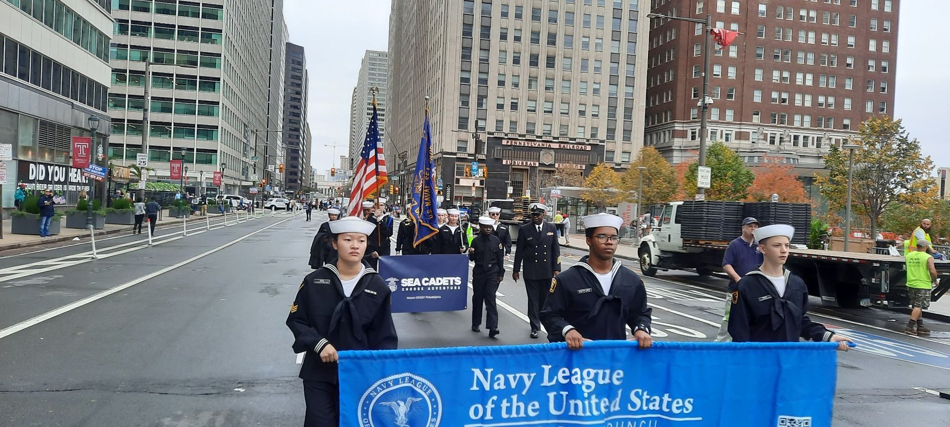 A group of people are holding a blue banner that says Navy League of The United States.