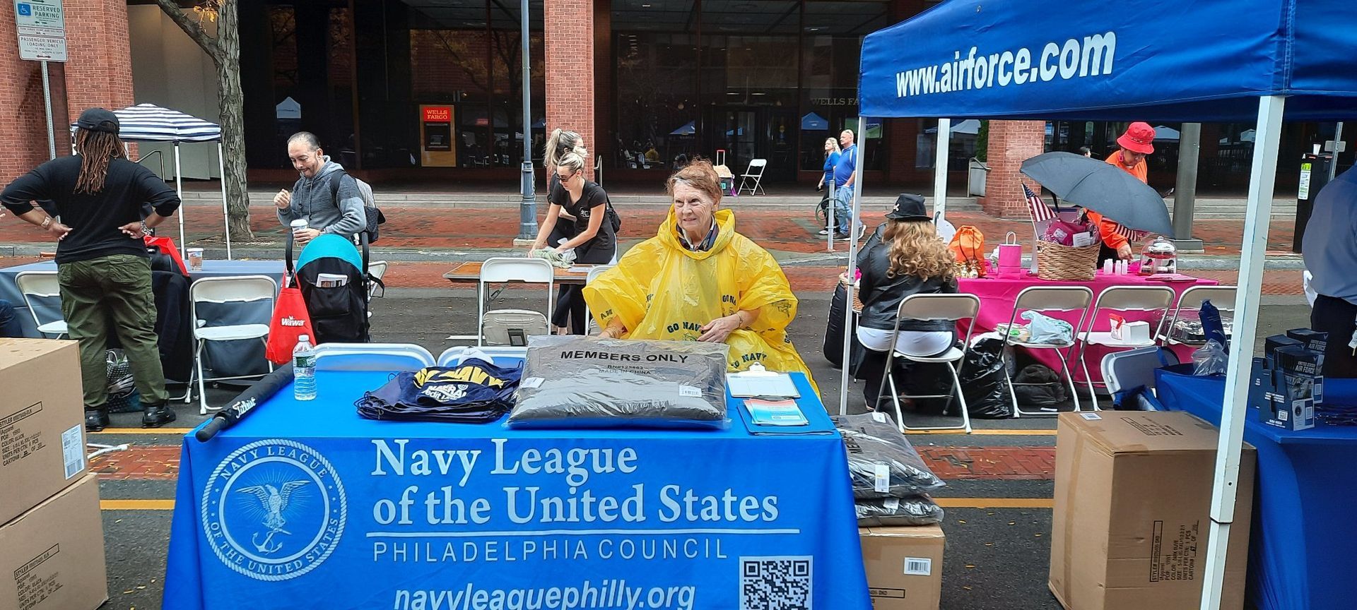 A man in a yellow raincoat stands behind a table that says Navy League of The United States