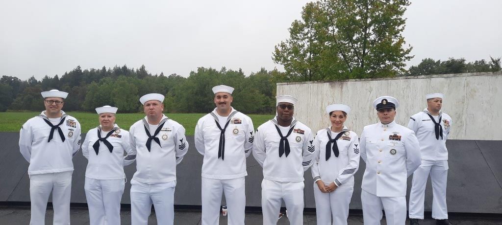A group of sailors in white uniforms are standing in a line
