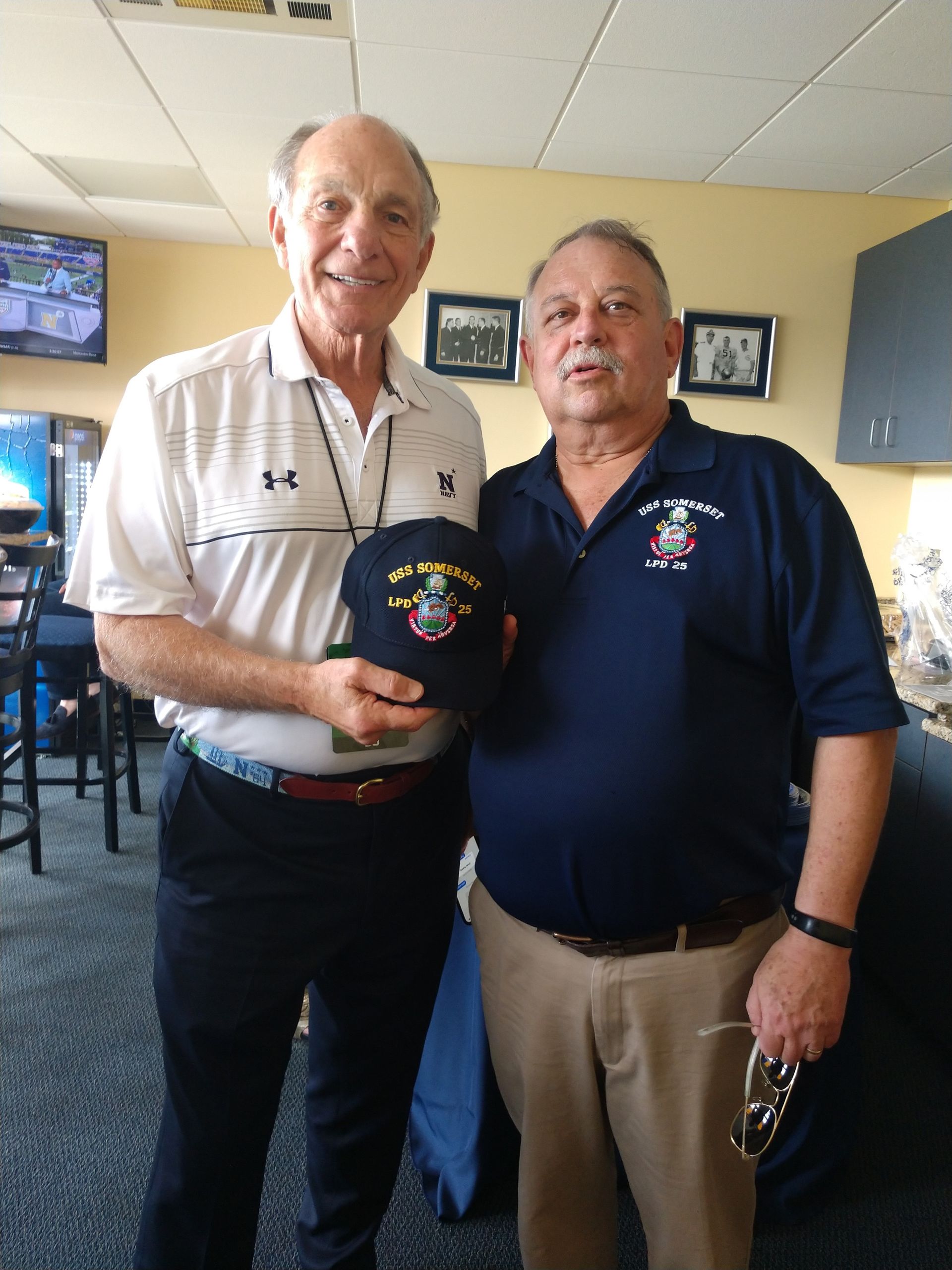 Two Men Are Posing for A Picture and One Is Holding a Hat that Says ' Us Marines ' on It