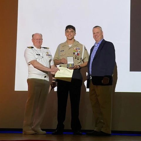 Three men are standing next to each other and one of them is holding a certificate
