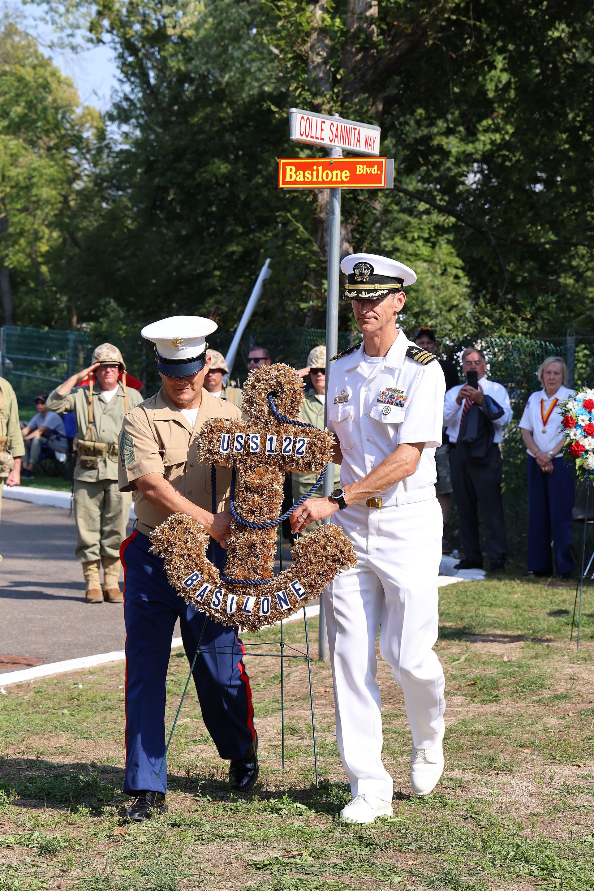 Two men in military uniforms are standing next to each other holding a wreath.