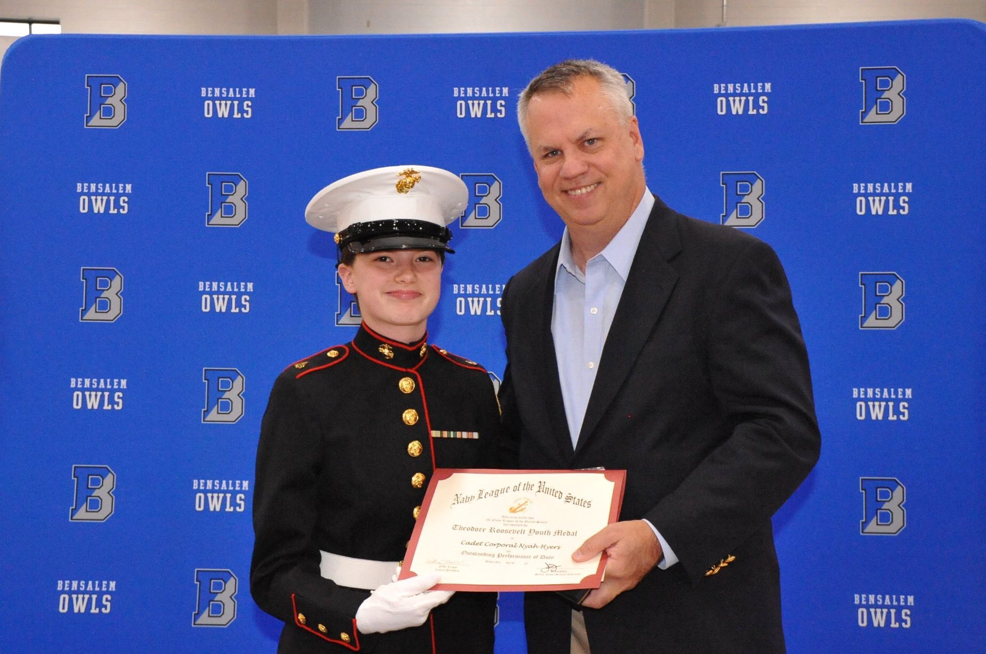 A man is holding a certificate next to a girl in a marine uniform