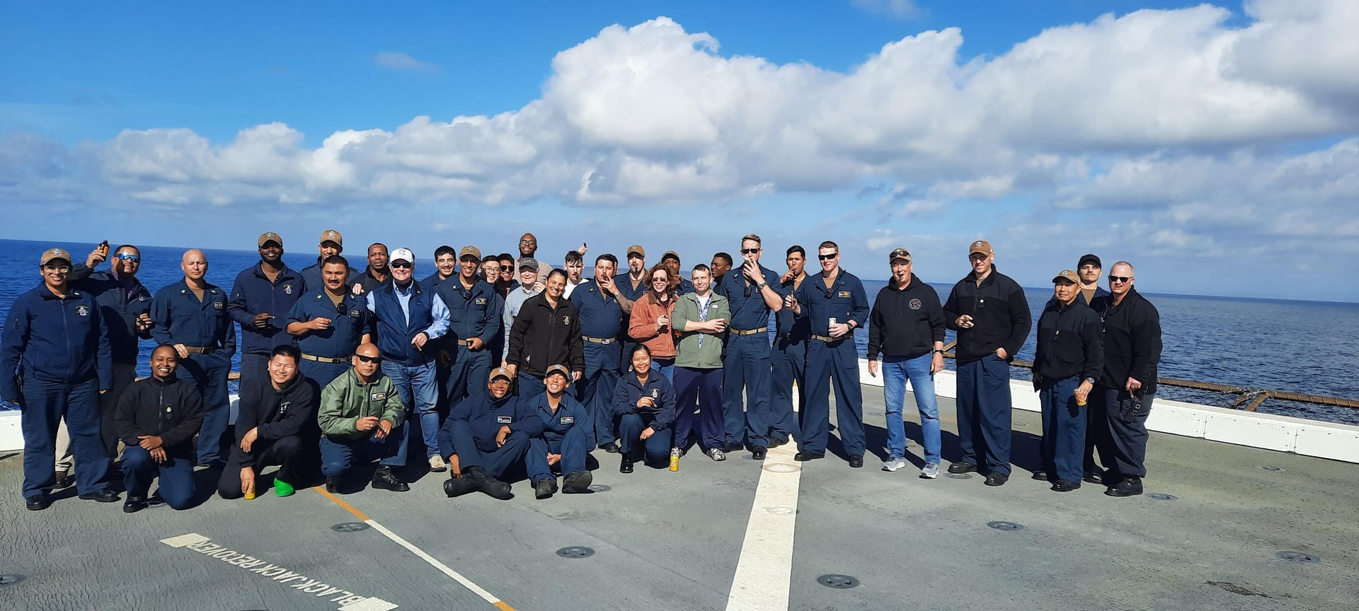 Three men are posing for a picture in front of a navy league banner