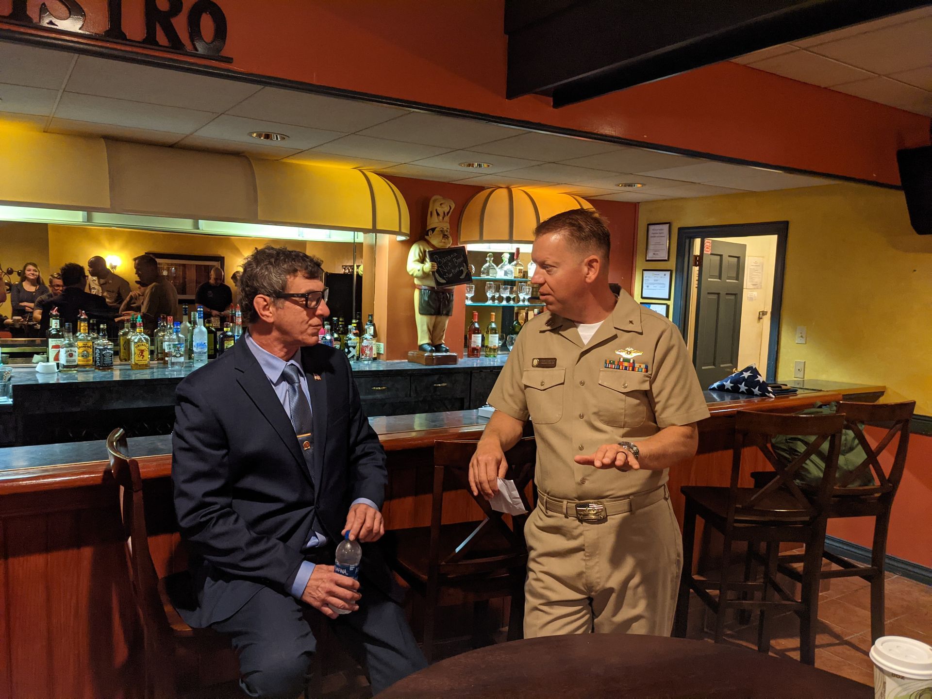 Two Men Are Sitting at A Table in A Bar Talking to Each Other