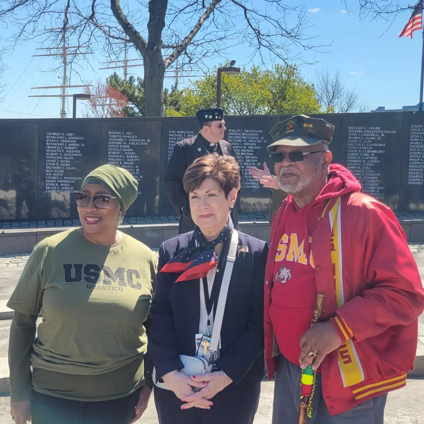 Three people are posing for a picture with one wearing a usmc shirt