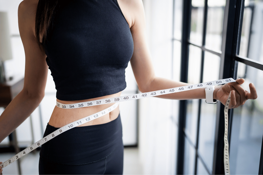 Woman in black athletic wear measuring waist with a tape measure.
