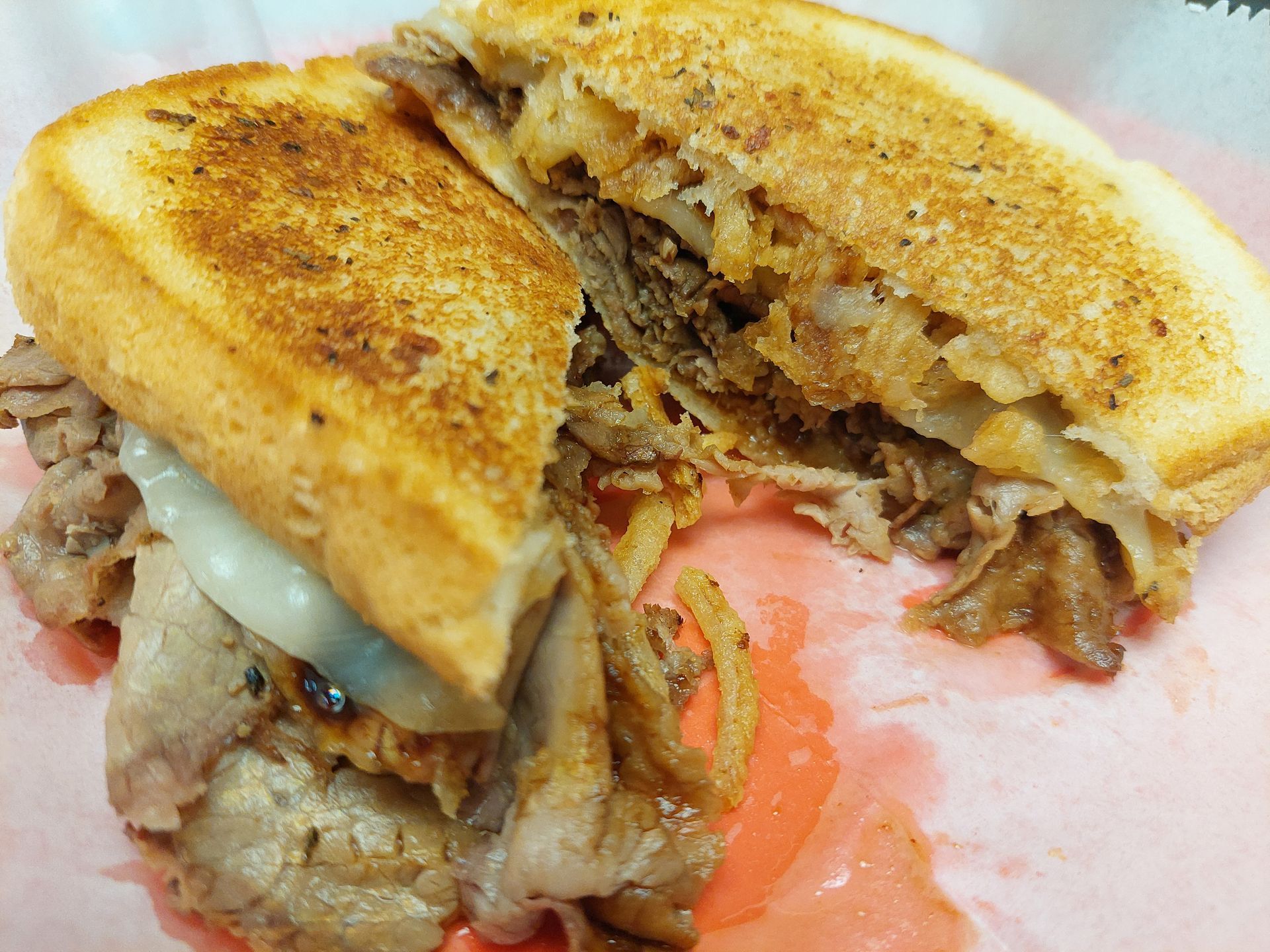 A grilled pork sandwich is cut in half on a piece of paper.