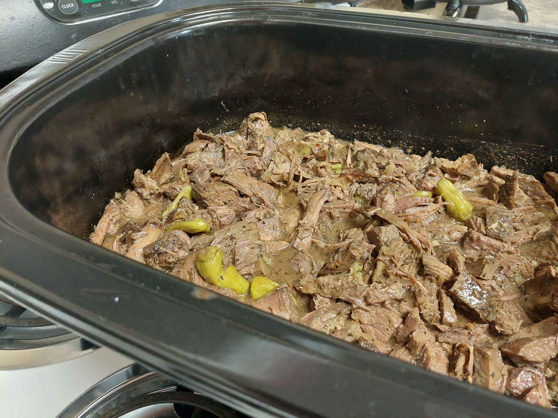 A crock pot filled with meat and peppers on a stove.