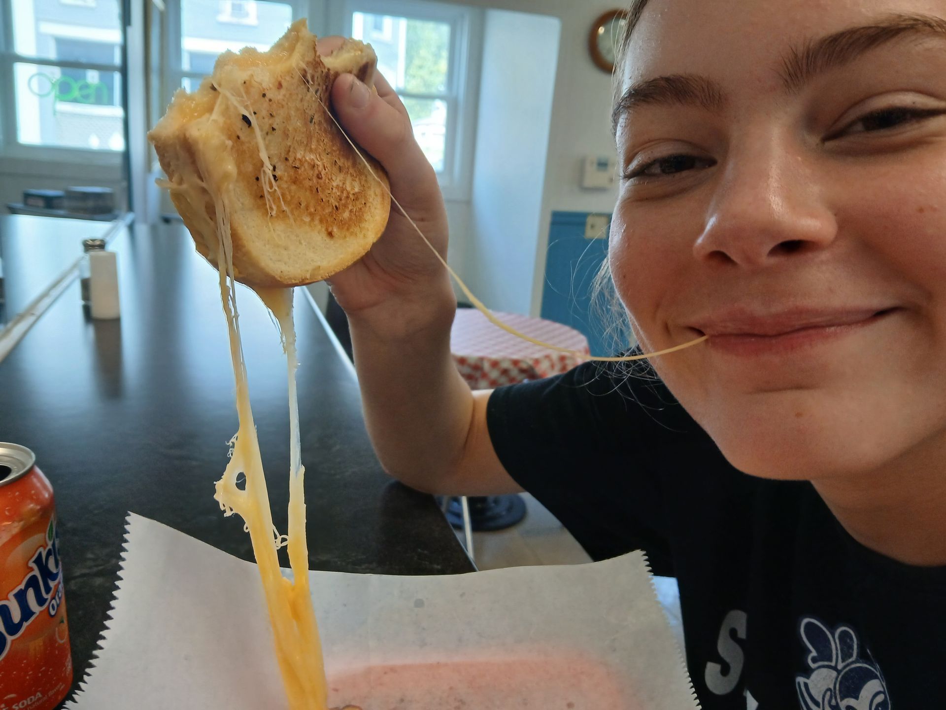 A girl is eating a grilled cheese sandwich next to a fanta can