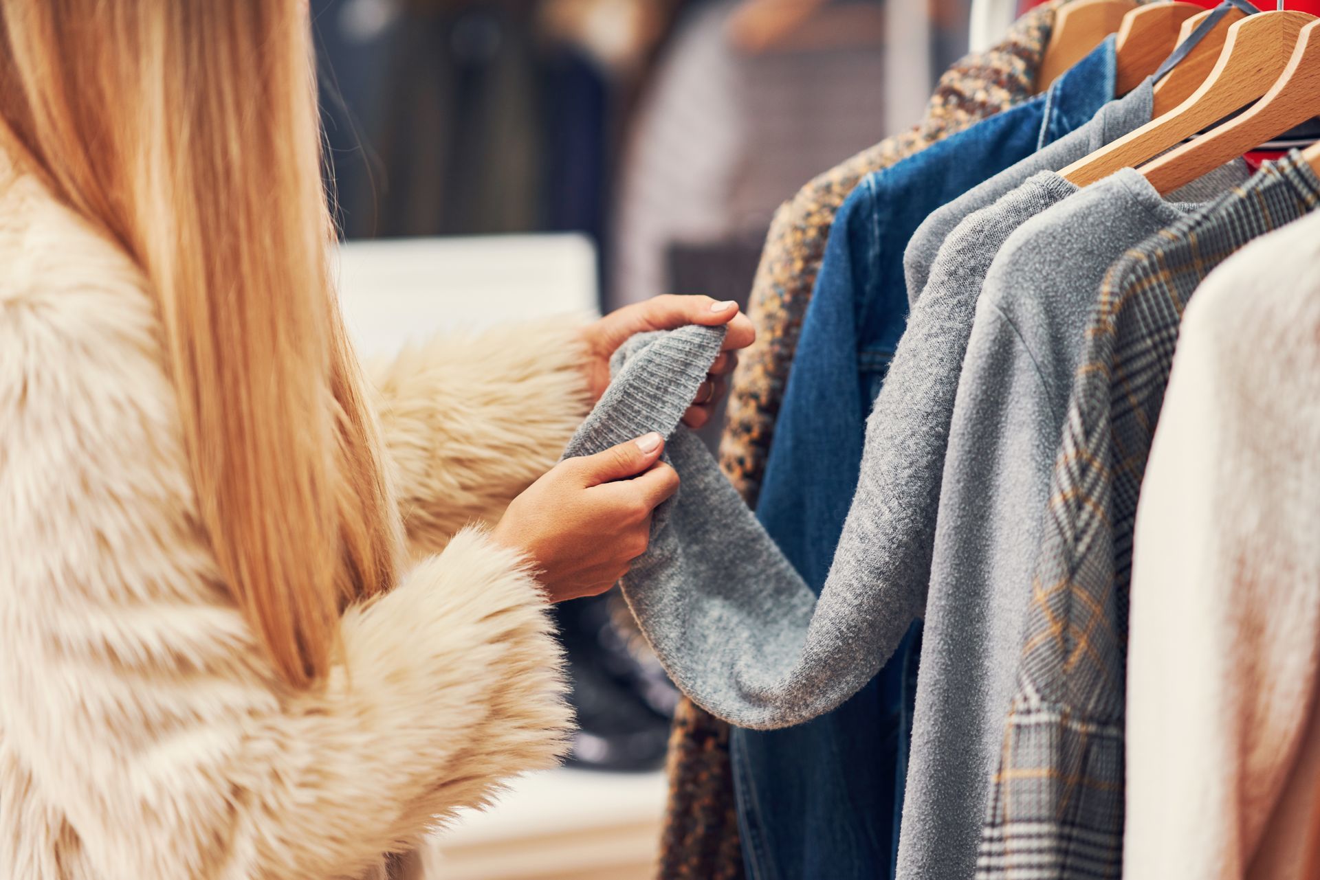 A woman is looking at a sweater hanging on a rack in a store.