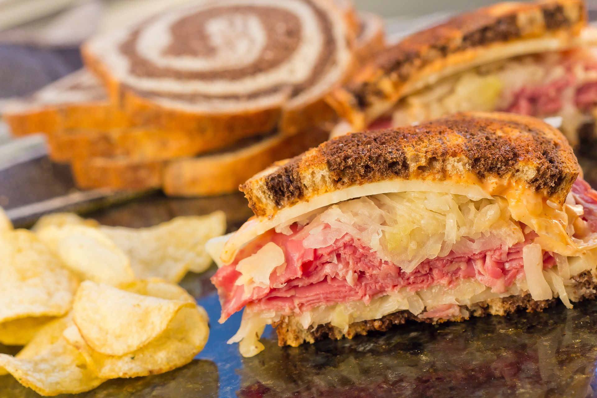 A corned beef sandwich is sitting on a table next to potato chips.