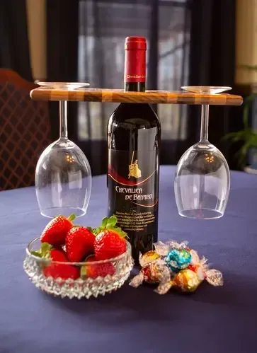 A bottle of wine is sitting on a table next to a bowl of strawberries and candy.