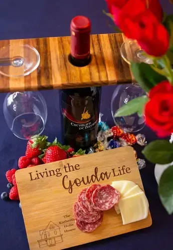 A wooden cutting board with a bottle of wine , cheese , salami and strawberries on it.