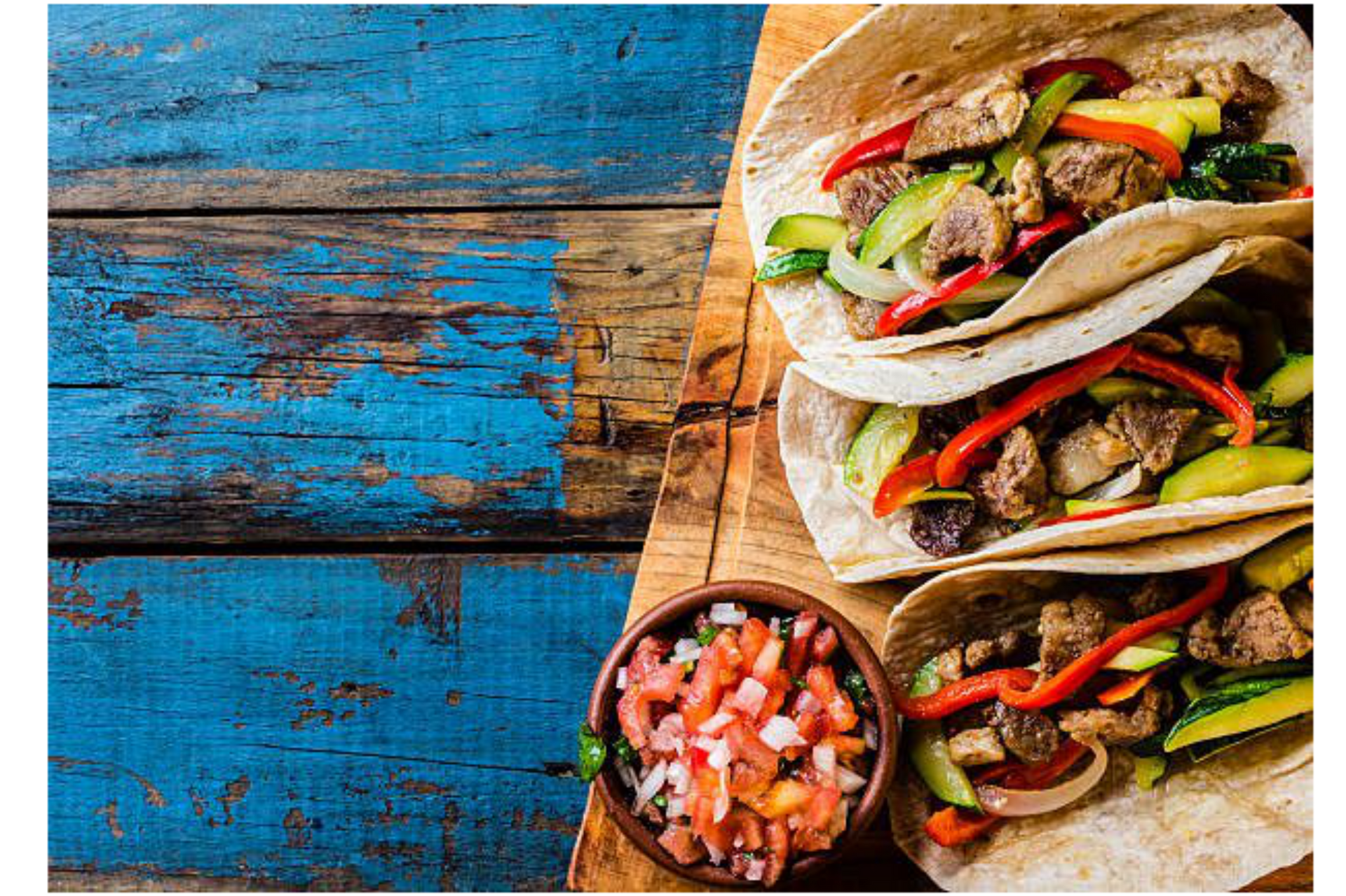 Three tacos are sitting on a wooden table next to a bowl of salsa.