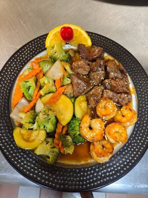 A plate of steak shrimp and vegetables with a cherry on top