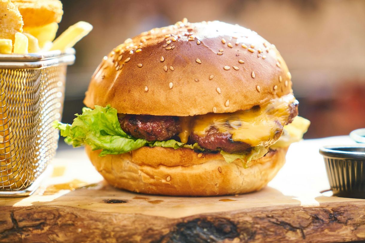 A hamburger is sitting on a wooden cutting board next to a basket of french fries.