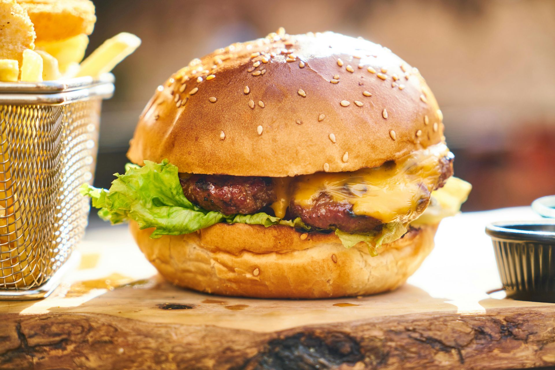 A hamburger is sitting on a wooden cutting board next to a basket of french fries.