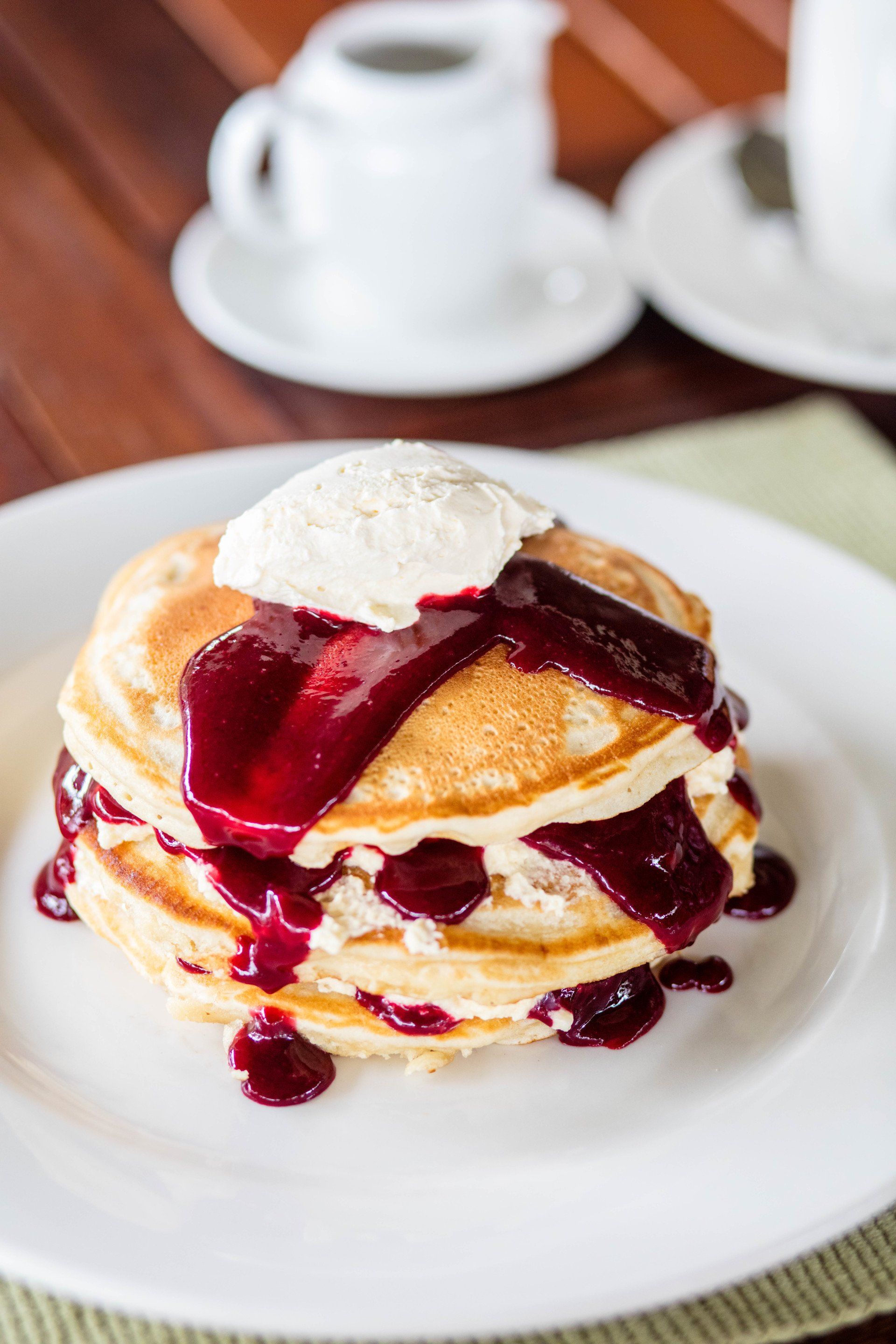 A stack of pancakes with berry sauce and whipped cream on a white plate.