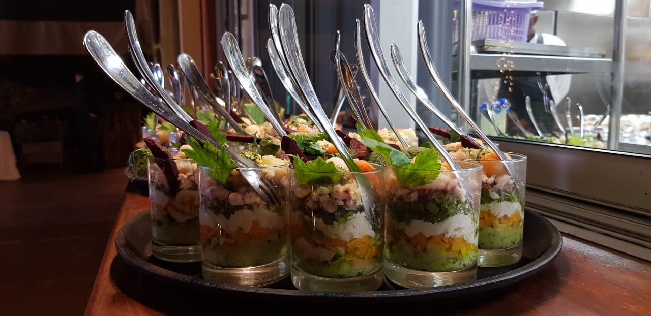 A tray of glasses filled with food and spoons on a table.