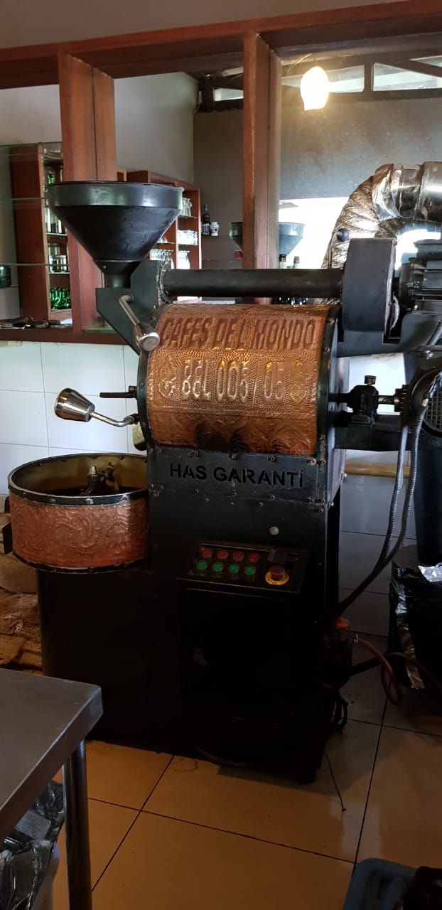 A coffee roaster is sitting in a room next to a coffee grinder.