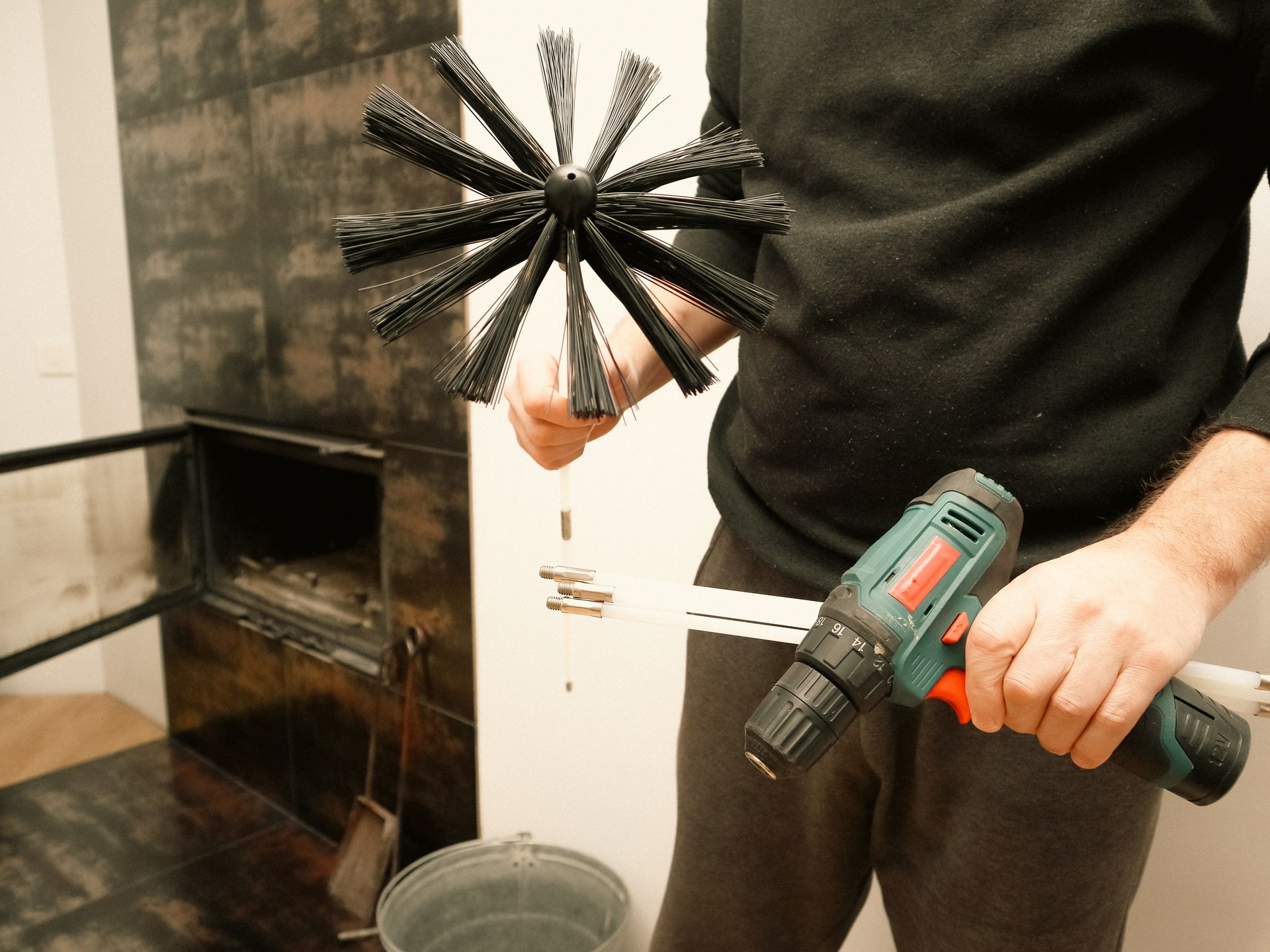 Person cleaning a fireplace chimney with a brush attached to a drill.