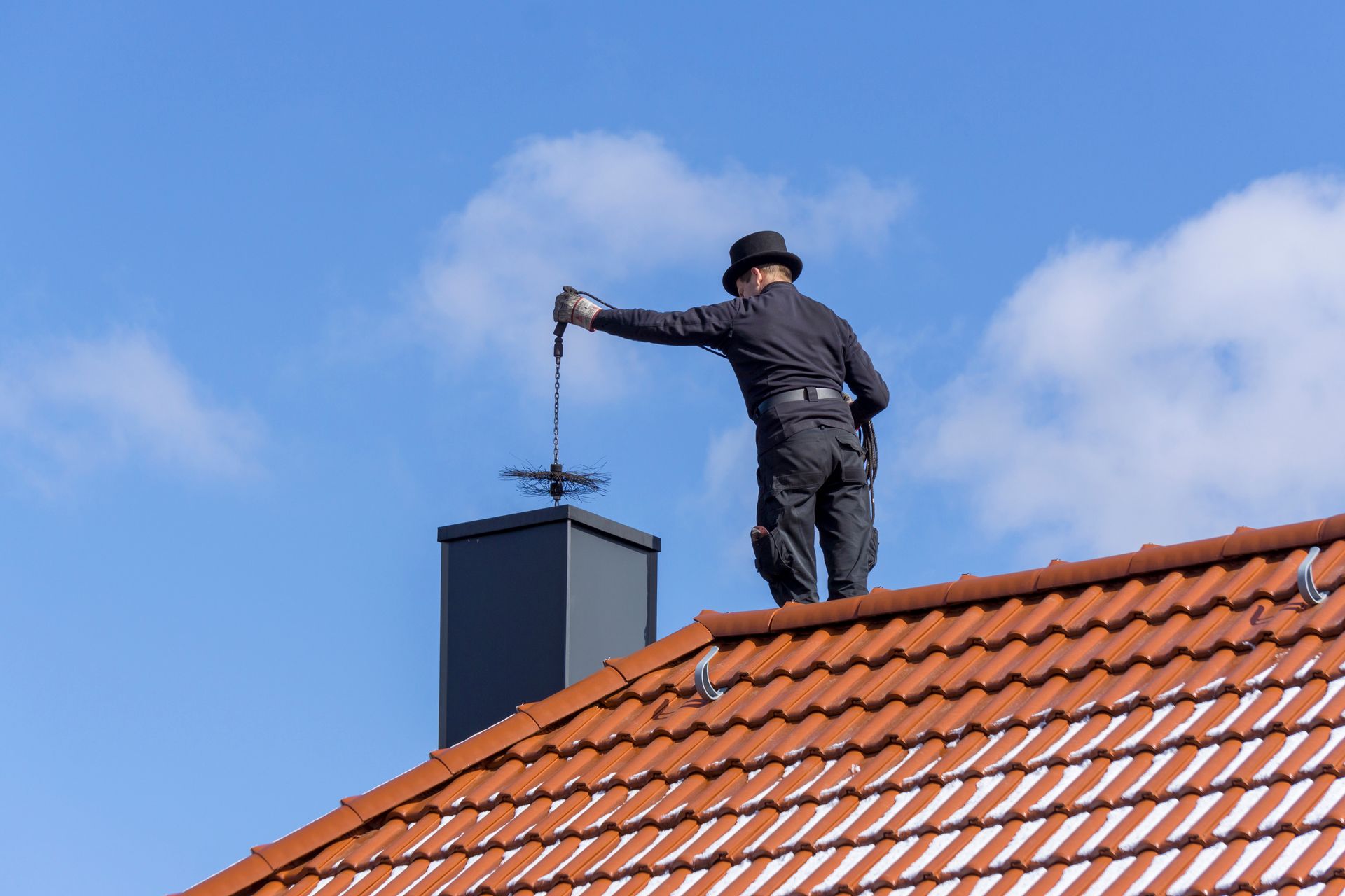 Chimney sweep on a roof, cleaning the chimney with a brush against a blue sky.