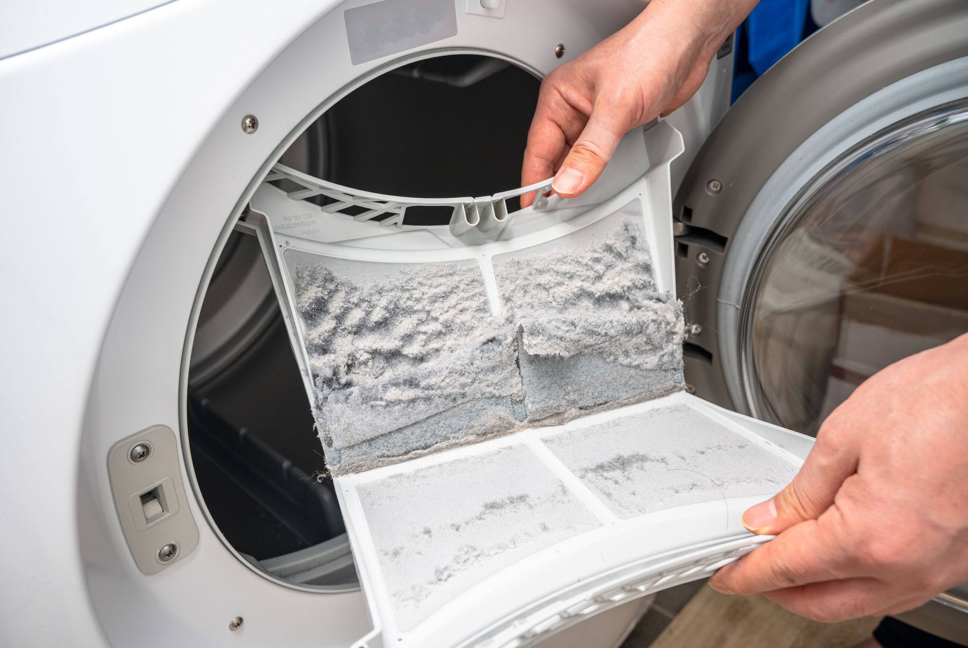 Person removing a lint-filled filter from a white dryer.