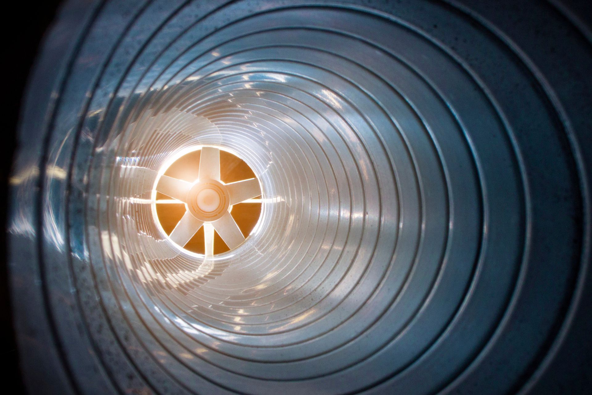 Inside view of a spiral ventilation duct with fan blades at the center, illuminated by warm light.