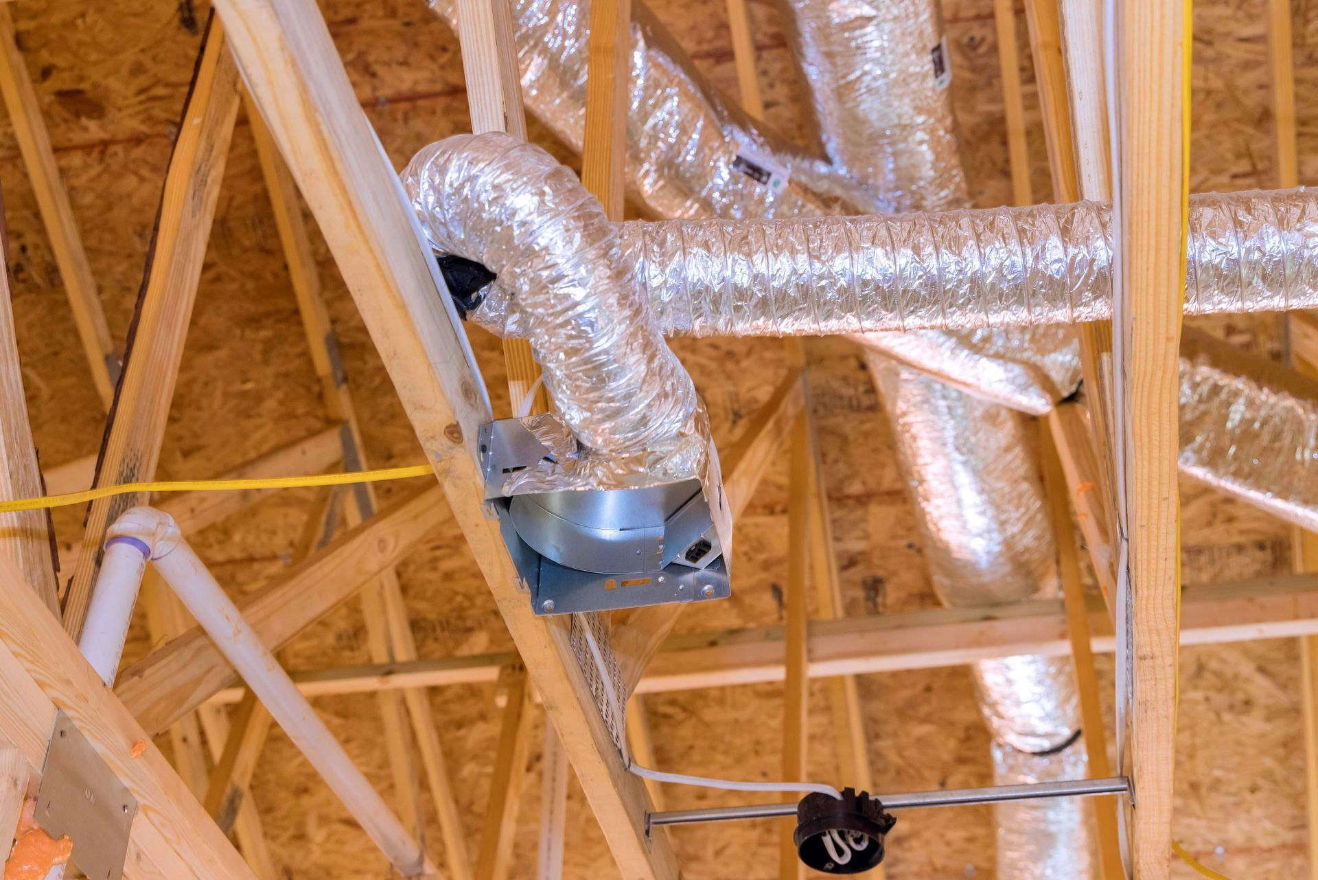 HVAC system in a wooden attic, with silver flex ducts and metal components visible.