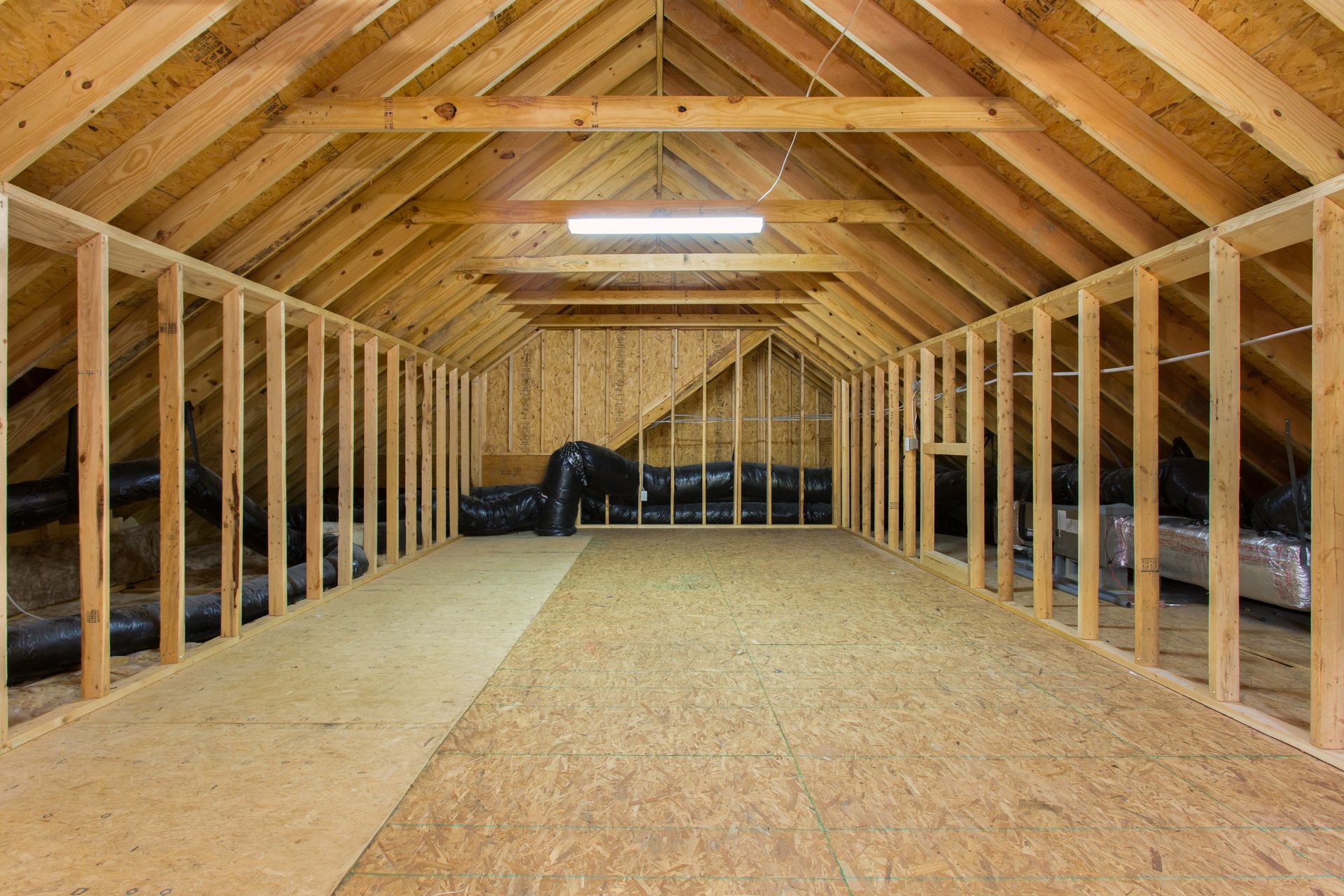 Interior view of a spacious unfinished attic with wooden beams, framing, and plywood flooring.