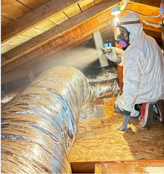 Man in an attic installing ductwork; wearing a hat, gloves, and overalls. Man in an attic installing ductwork; wearing a hat, gloves, and overalls.