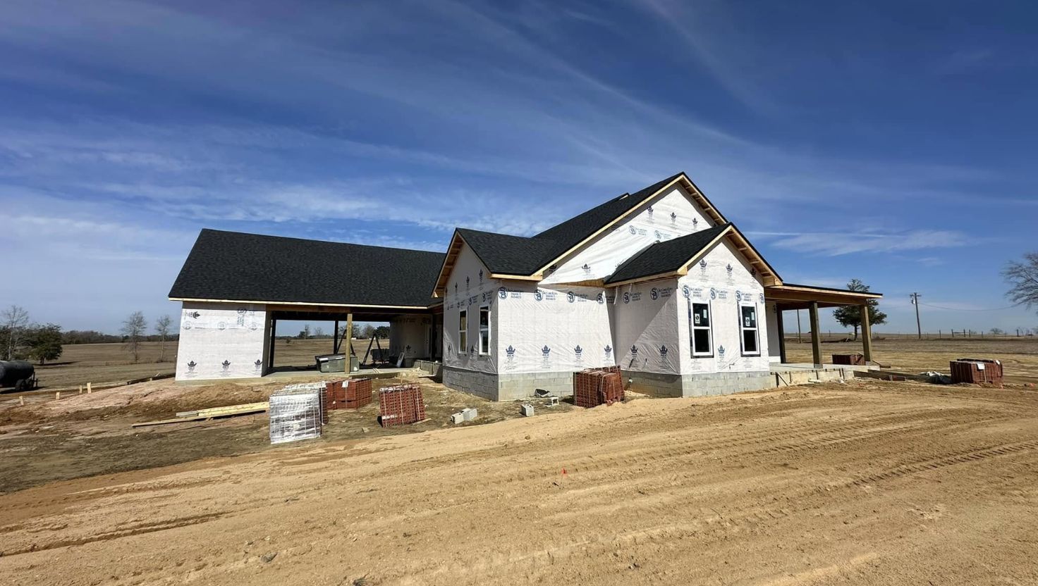 House under construction with attached carport, blue sky, and brown dirt.