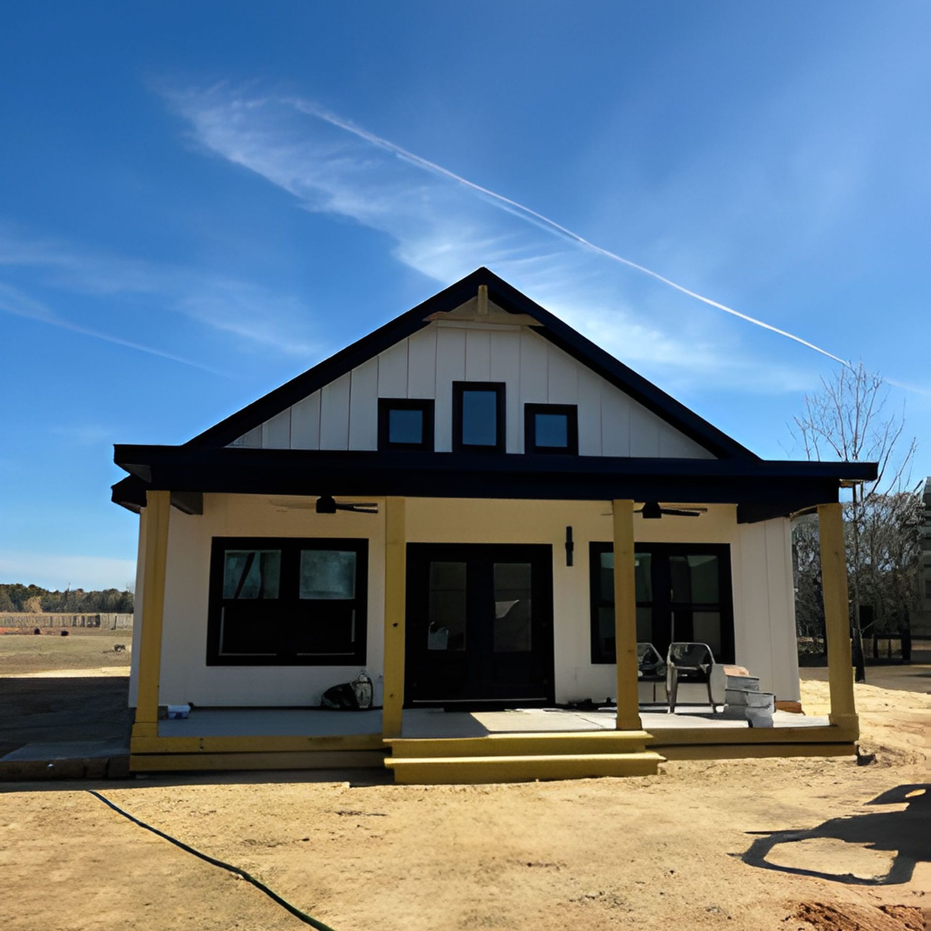 White and black farmhouse style house under construction; blue sky.
