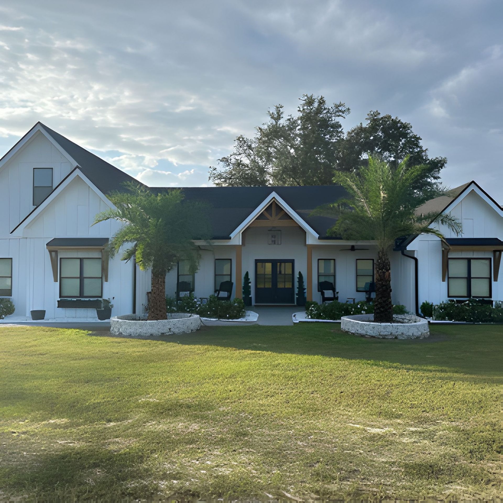White farmhouse with black trim and roof, two palm trees, and green lawn.