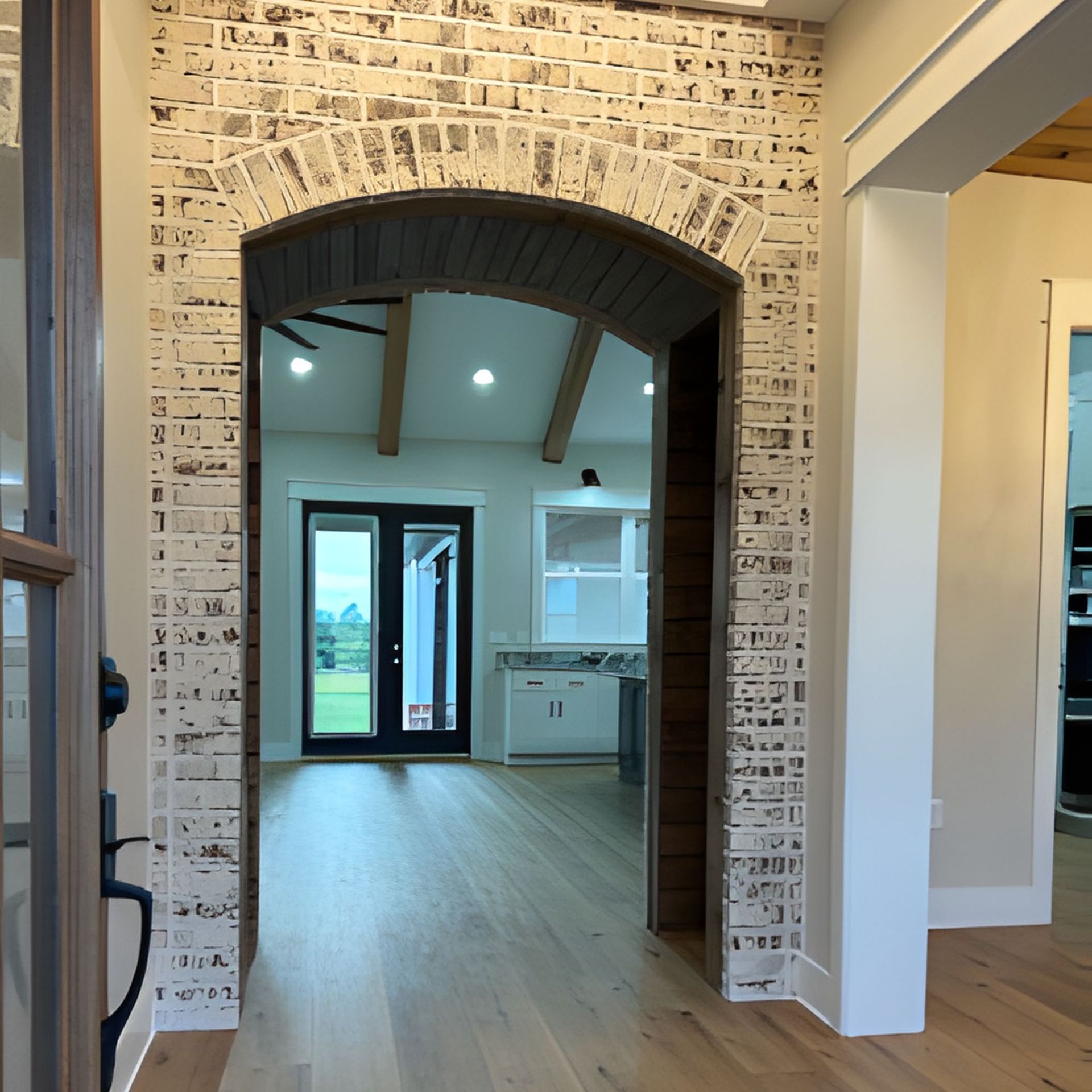 Arched doorway with white brick. Interior view: wood floor, open to a kitchen with cabinets, and exterior doors.