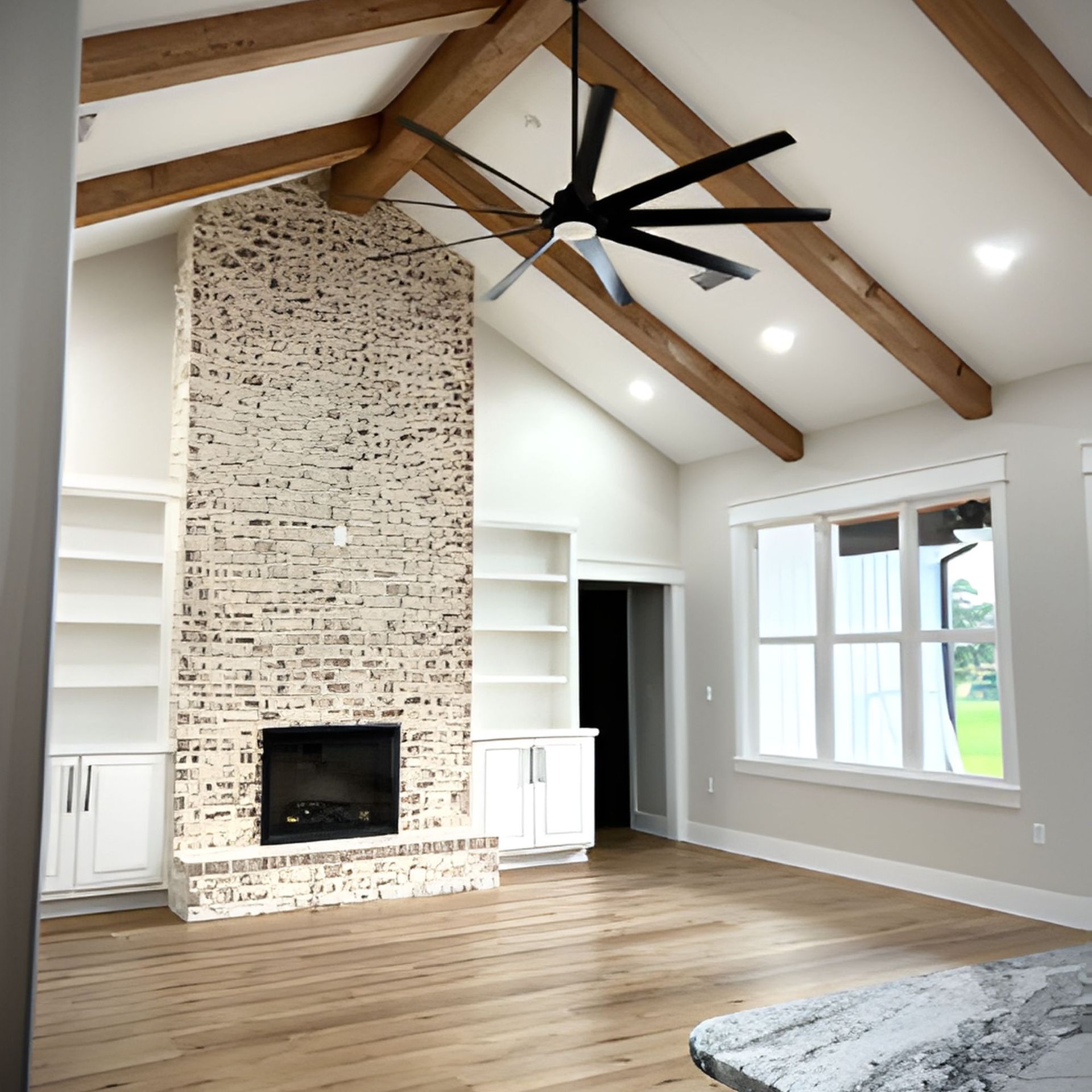 Living room with a brick fireplace, built-in shelves, wood beams, a ceiling fan, and large windows.