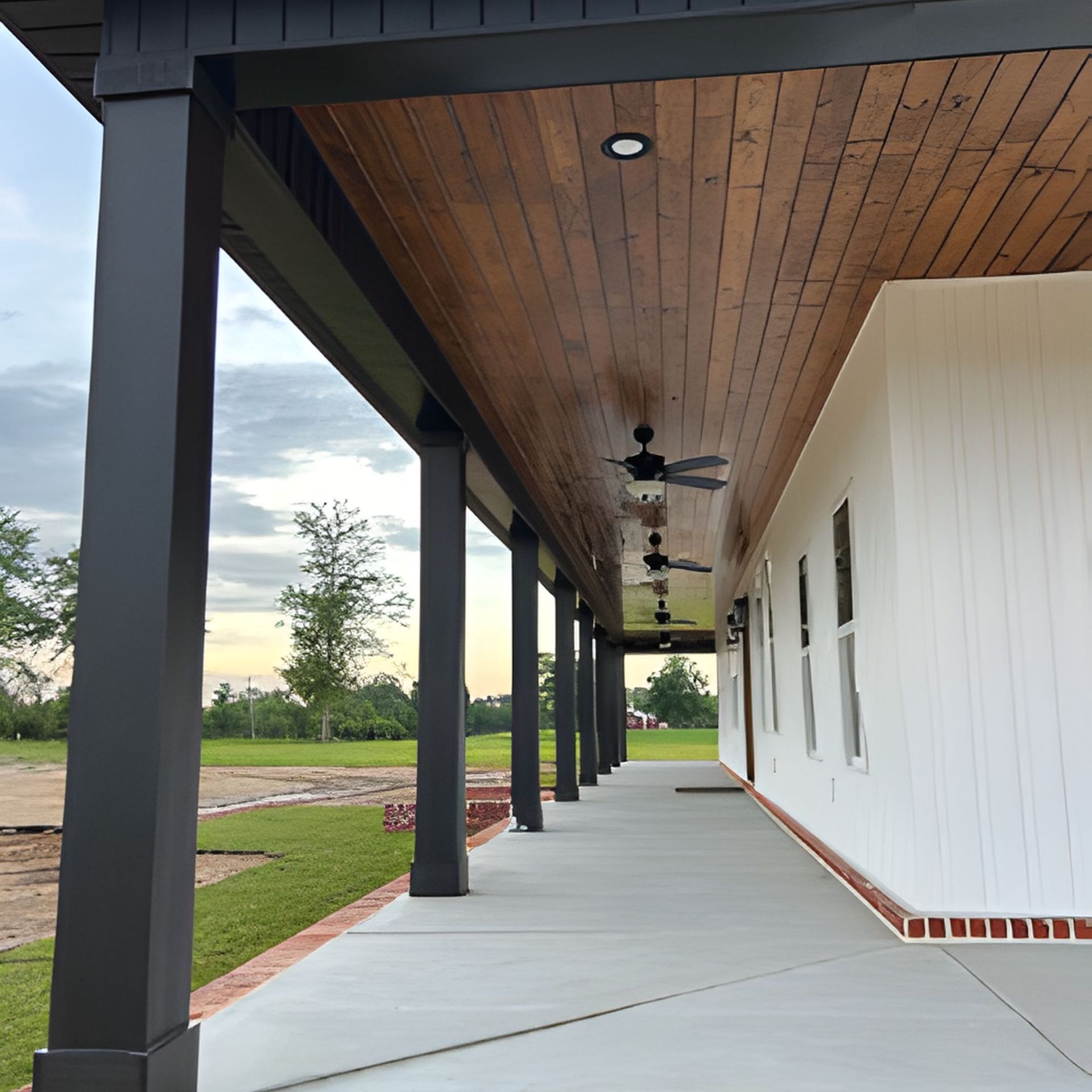Covered porch with black columns, brown ceiling, white siding, and concrete walkway.