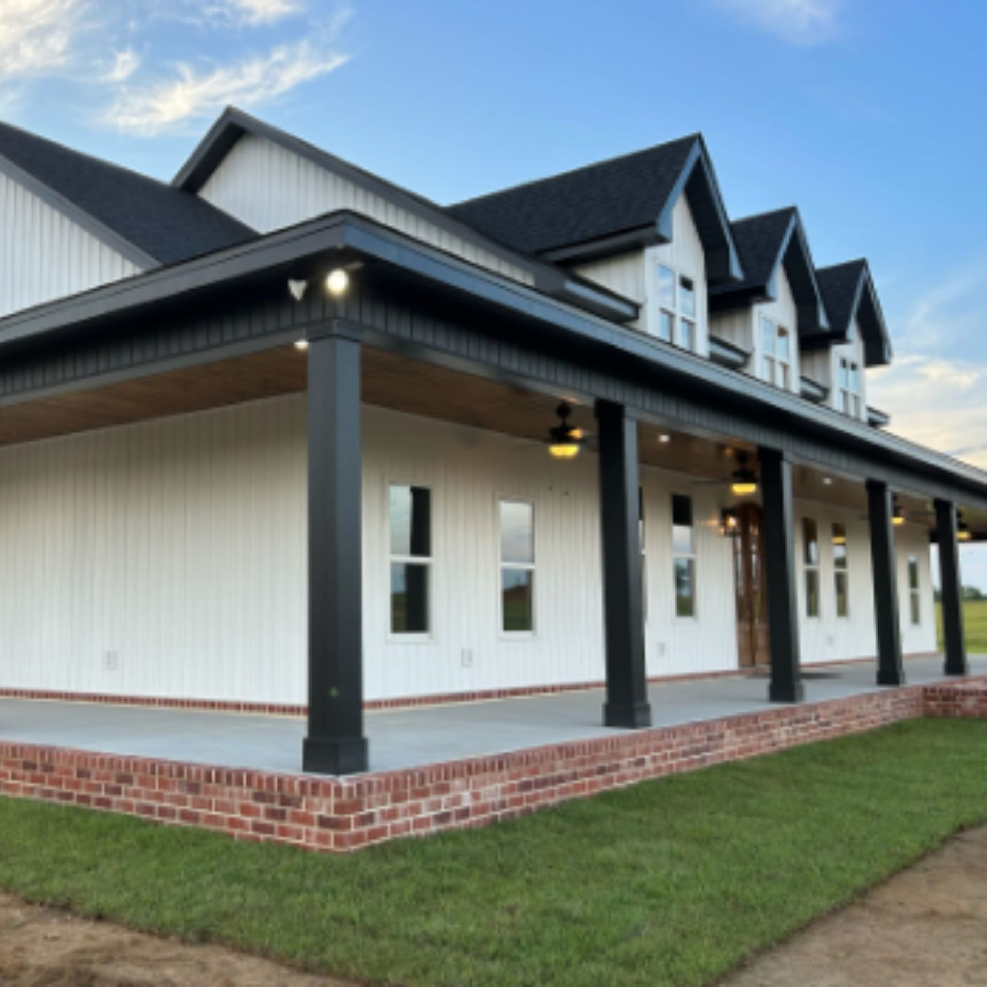 White farmhouse with black trim, a brick base, and a large front porch.