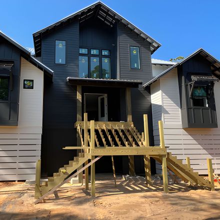 Black and white modern house under construction. Wooden stairs lead to the front door.