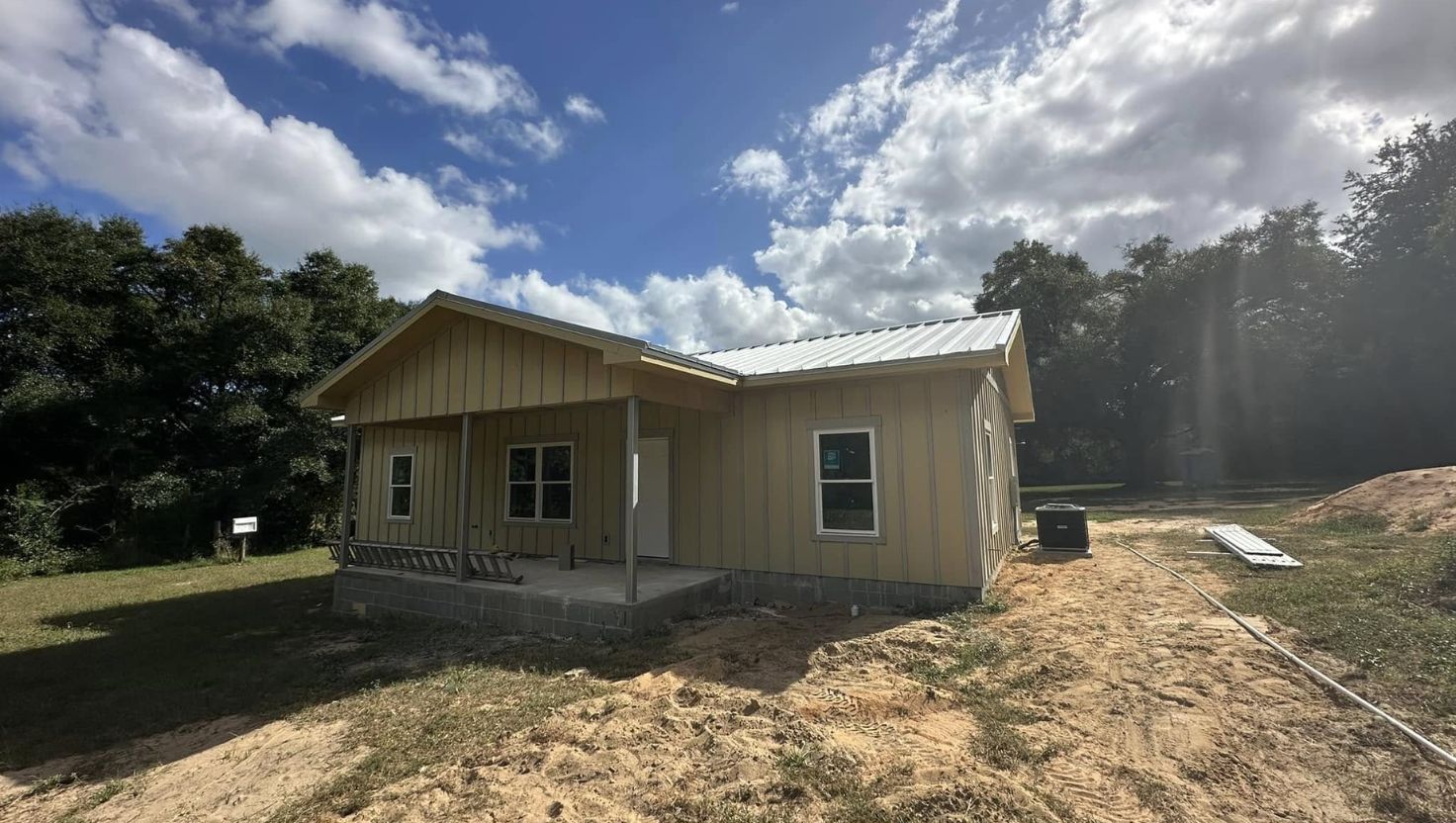 New construction house with tan siding, metal roof, and covered porch under a cloudy sky.