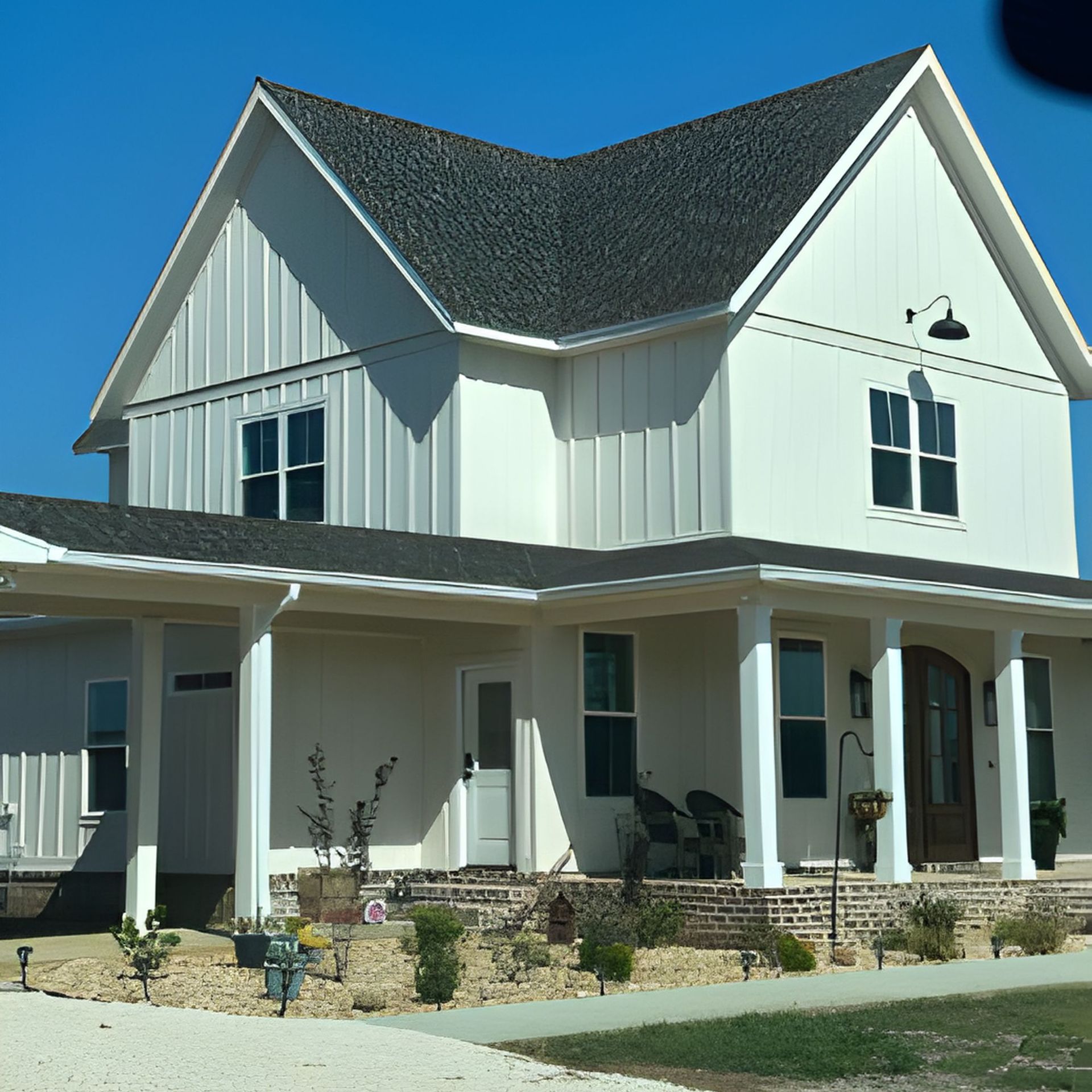 White farmhouse with black roof and covered porch against a clear blue sky.