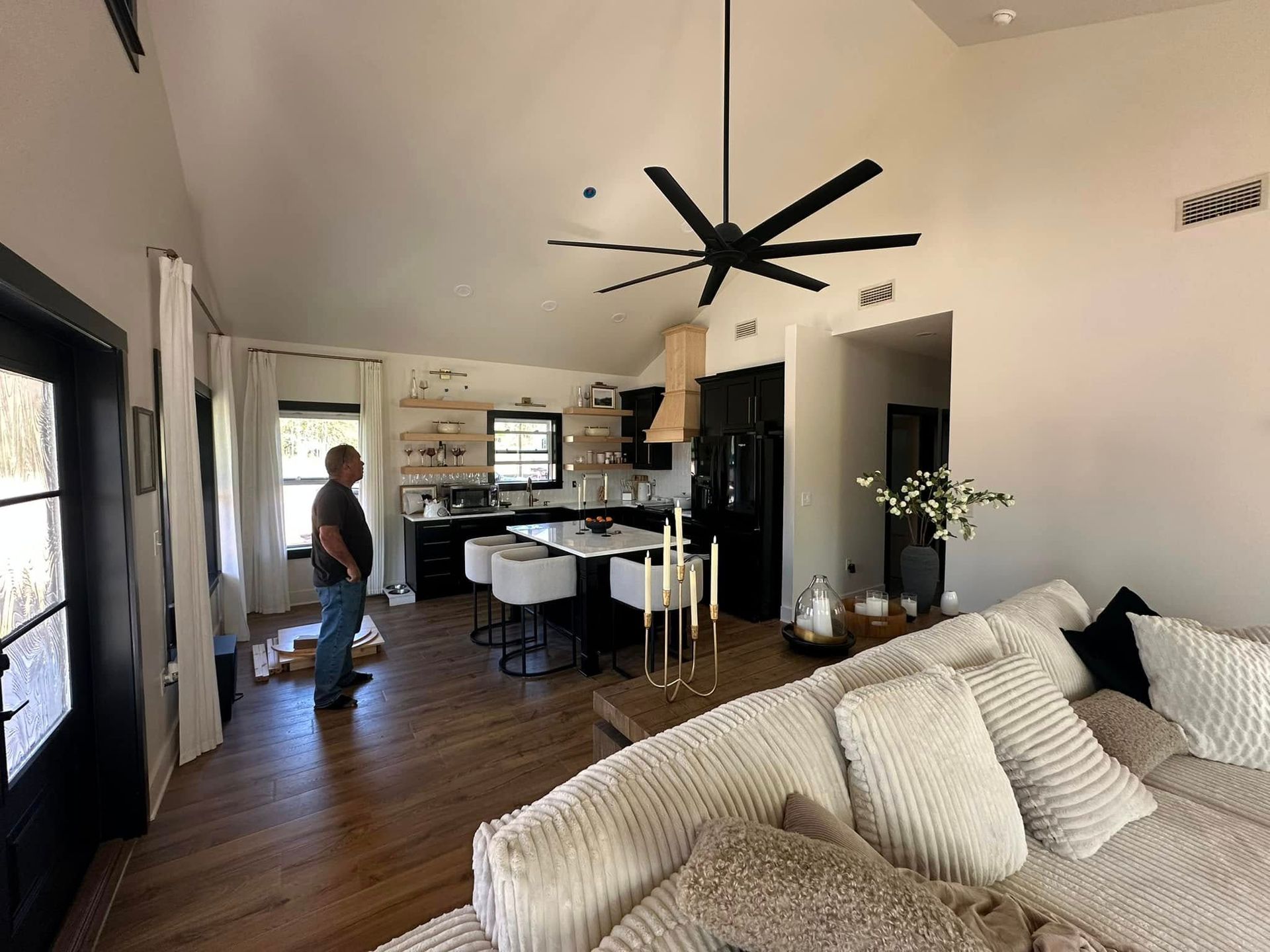 A man is standing in a living room with a couch and a ceiling fan.