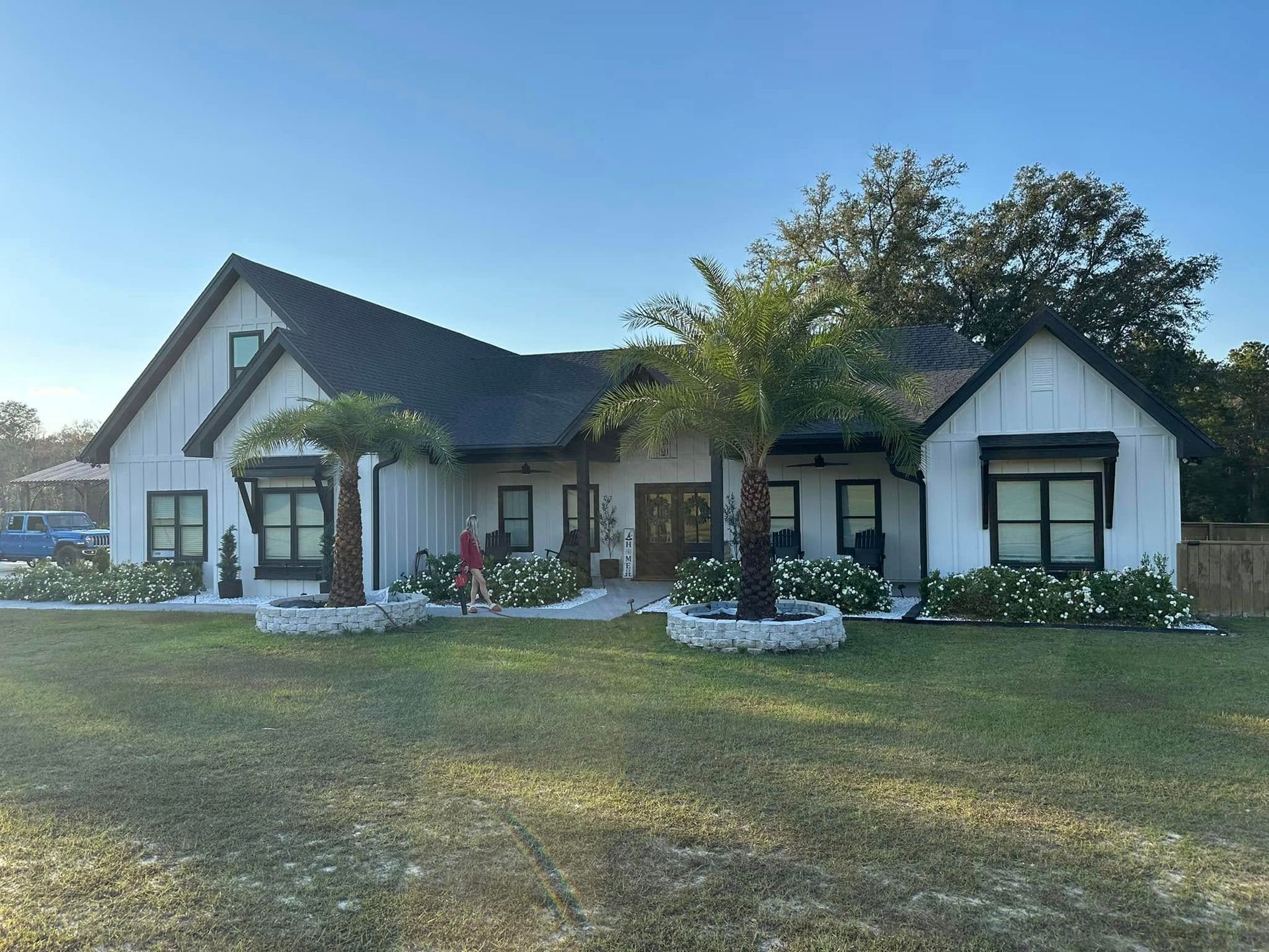 A large white house with a black roof and palm trees in front of it.